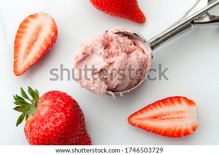 Refreshing cold sweets, seasonal dessert and cool summertime treat concept with close up on scoop of vivid pink strawberry ice cream and scattered strawberries isolated on white marble background