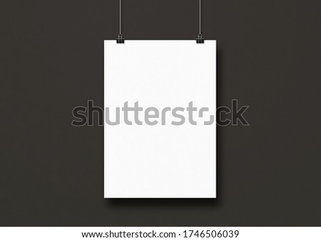White poster hanging on a black wall with clips. Blank mockup template