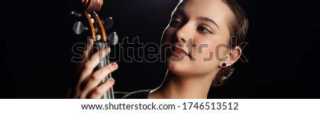 attractive professional musician looking at violin isolated on black, horizontal crop