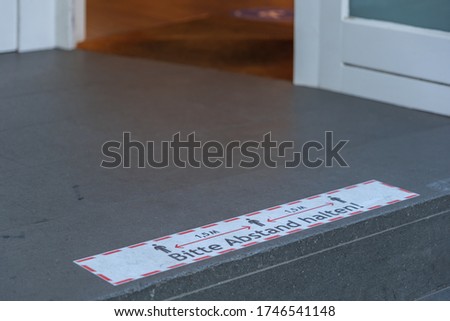 Selected focus low angle view at " 1.5m Abstand halten " means "keep 1.5m distance", on rectangular caution sign on the floor in front of entrance of store in Germany during epidemic of COVID-19.