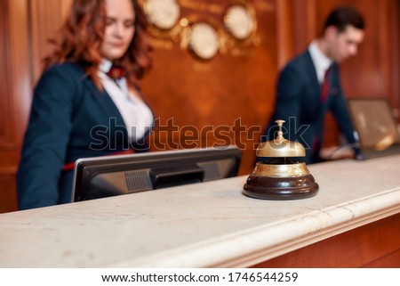 Attractive executives at the reception desk of a hotel in the background. Focus on a service bell. Horizontal shot