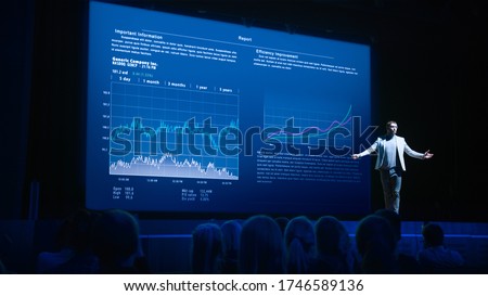 Business Forum Economics Conference Stage: Professional Speaker Concludes His Report with a Speech and Showing Infographics, Statistics on the Big Screen.