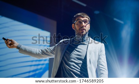 Inspirational Male Speaker Does Presentation of New Technological Product, Shows Infographics, Statistics Animation on Big Screen, Talks About Device Performance. Live Event / Start-up Conference Royalty-Free Stock Photo #1746589205