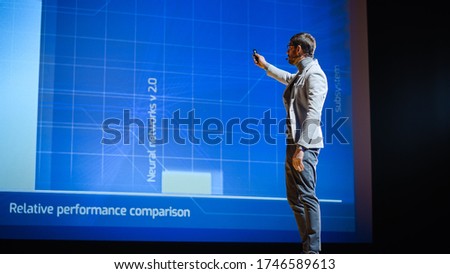 Male Speaker Stands on Stage and Does Presentation of the Technological Product, Shows Infographics, Statistics Animation on Screen. Live Event / Device Release / Start-up Conference