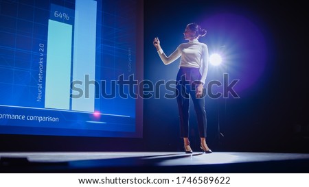 On-Stage Successful Female Speaker Presents Technological Product, Uses Remote Control for Presentation, Showing Infographics, Statistics Animation on Big Screen. Live Event / Business Conference