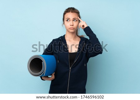 Teenager Russian girl holding mat isolated on blue background having doubts and thinking
