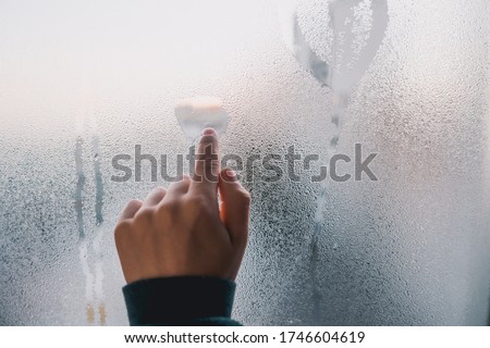 Closeup on child hand draws on misted and wet window. Emotional human belief in best. Homescooling isolation. Natural refreshing drops on glass