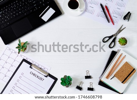 Frame of white wooden office desk table background with laptop, supplies, notepad, checklist, green plants, eye glasses, calendar, credit card and cup of coffee. Top view with copy space