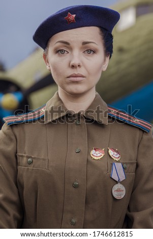 A young female pilot in uniform of Soviet Army pilots during the World War II. Military shirt with shoulder straps of a major and a beret. Against the background of a military aircraft.
