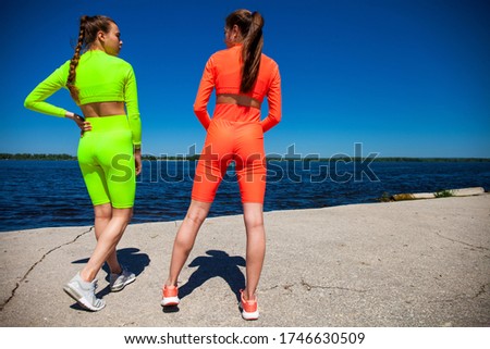 Full body portrait of a young beautiful fitness models in sportswear trains against the blue sky