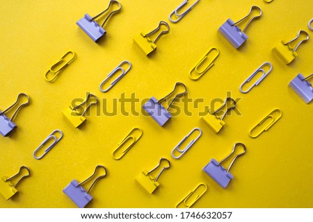 
Colorful background with office supplies. Paper clips and paper clips are on a bright yellow background - top view of a flat lay. The concept of a new school year at school.