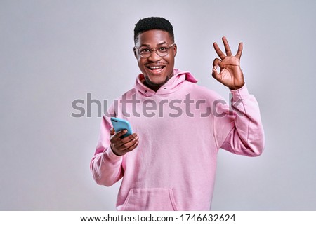 Young african american man using smartphone doing ok sign with fingers, excellent symbol on grey background. Copy space