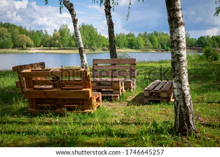 Rustic wooden table and benches made with pallets on the shore of a tranquil a lake surrounded by trees and greenery in summer sunshine Royalty-Free Stock Photo #1746645257