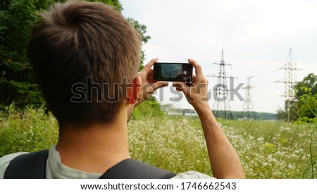 Adult man taking a picture with smart phone. Outdoor shot in nature. Shallow depth of field. Back view