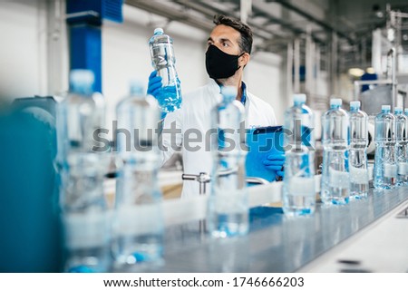 Male worker in workwear and with protective mask on his face working in bottling factory. Inspection quality control. 