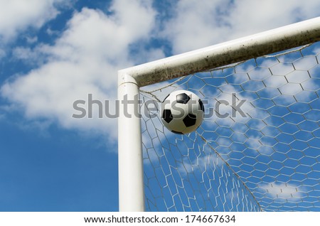 Close-up of a soccer ball (football) going into the top corner of the goal with a blue sky background.
