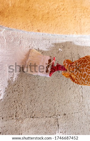 
Painting a cement wall with white paint using a brush. Yellow gloves with a giraffe pattern.