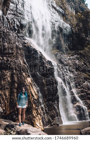Young blue haired girl standing under Diyaluma waterfall in Sri Lanka. White tourist in Asia enjoying vacation during high season. Adventure traveler exploring the world. Beautiful outdoor picture.