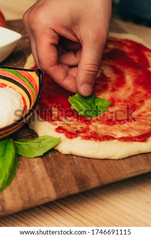 Stock photo of a pizza dough with one hand placing a basil leaf. Mozzarella, basil, tomato and oil around the dough.
