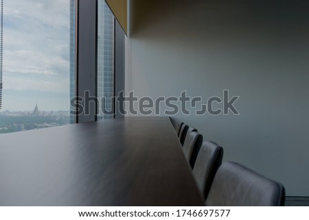Stylish office on the 45th floor of the tower. A large long table near a number of panoramic windows. A magical view from a large window. Clean comfortable place. A row of chairs.