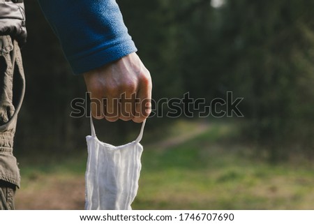 Man takes off mask after quarantine, enjoys walking in forest alone. End of  coronavirus, lockdown, beginning of normal life. Close up view of hand with mask. View from behind. Quarantine over concept