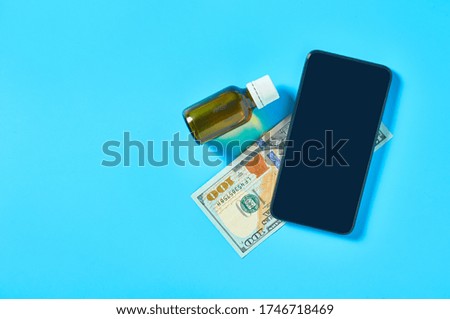 Smartphone near bottle with vaccine and banknote of one hundred dollars on blue background. E-health, e-medicine, payment for services concept. Online purchasing, consultation, medical assistance