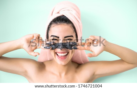 Happy smiling girl applying facial charcoal mask portrait - Young woman having skin care cleanser spa day - Healthy beauty clean treatment and cosmetology products concept - Aquamarine background Royalty-Free Stock Photo #1746721004