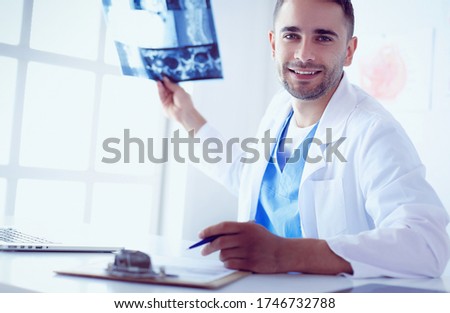 Young doctor sitting at his office desk and analyzing an x-ray
