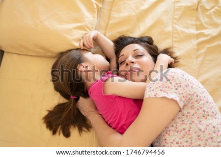 Mother and daughter hugging each other while sharing a bed and cosleeping at home