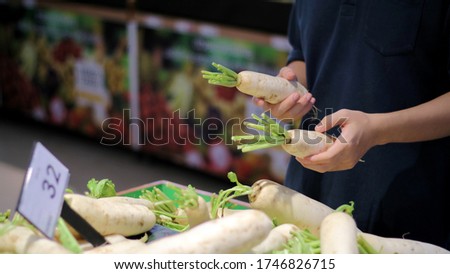 A man choosing, selecting or comparing vegetable (white radish daikon) on stall with price tag at supermarket
