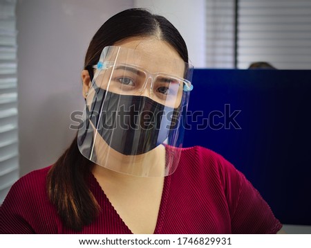 A young and beautiful Asian woman wearing a surgical mask and face shield to protect against Covid-19 while working in an office. Royalty-Free Stock Photo #1746829931