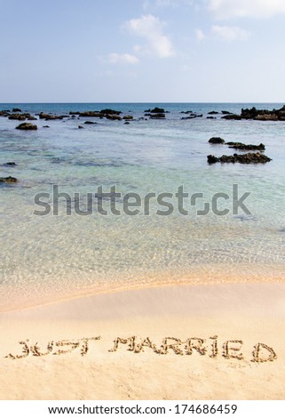Just Married written in sand on a beautiful beach, blue clear waves in background