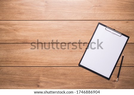 Clipboard with note-taking paper and pencils placed on a wooden desk.