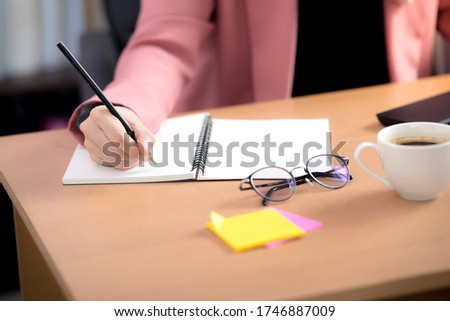Asian Muslim woman office worker sitting in front of laptop computer at desk and taking notes at office.