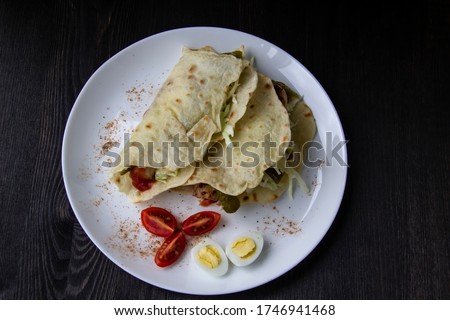 Sliced ​​chicken with canned  cucumbers and cabbage in sauce, wrapped in pita bread on a white plate. Delicious for lunch or dinner. Pieces of tomato and eggs on a plate with pita bread