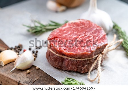 Raw beef filet Mignon steak on a wooden Board on paper with ingredients for grilling, close up Royalty-Free Stock Photo #1746941597