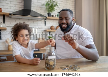Saving money. Dark-skinned bearded man holding a coin into his hand Royalty-Free Stock Photo #1746943916