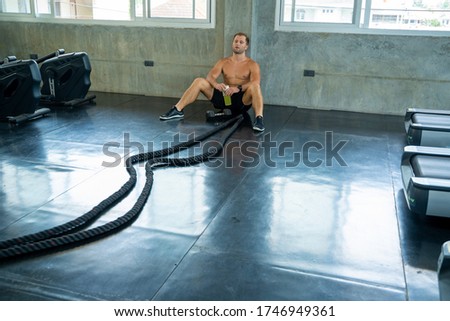 Muscular young man is exercising with battle rope in training fitness gym,Tired and exhausted man resting after intense training session.