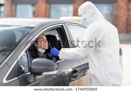 medicine, quarantine and pandemic concept - doctor or healthcare worker in protective gear or hazmat suit with cotton swab making coronavirus test for young woman in her car Royalty-Free Stock Photo #1746950069