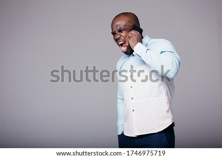 Black man in a white shirt yells at the interlocutor on the phone while holding his hand in his pocket in the studio.