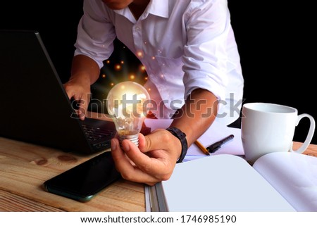 A man in a white shirt stretched out with one hand holding a shining lamp. And the other side pressing the notebook keyboard, creative concept with sparkling light bulbs