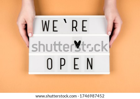 We're open text on a lightbox on an orange background in women's hands. A message from the owner of a business, cafe, or beauty salon.