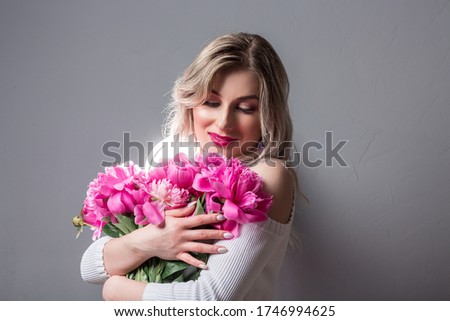 Beauty and body care. Photo of blonde girl with pink peonies on grey background.
