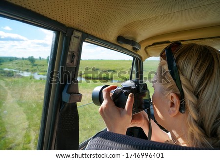 woman traveler photographer holding in his hands the camera, takes a shot of summer river and meadow from the car window. I do my work sitting in the car.photo through the car window. travel for photo