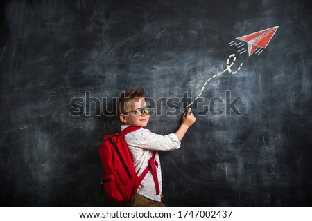Back to school. Kid with red bag against blackboard. Picture of drawn airplane