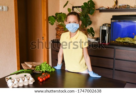 little girl with laptop. young woman holding blank sign. Coronavirus. Woman with face mask on quarantine, cooks in the kitchen at home during coronavirus crisis. Stay at home. Enjoy cooking at home. 