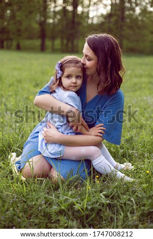 mom and daughter are sitting on a green meadow in blue dresses