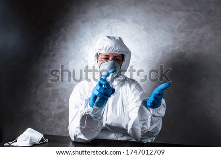 A nurse in a medical face mask and viral protective suit.. The doctor is sitting at the table in a medical face mask and a viral protective suit. The doctor disinfects the hands.