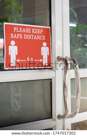 Red sign printed "PLEASE KEEP SAFE DISTANCE 6 ft" on the door office. New normal after covid-19 pandemic with social distancing.