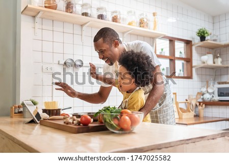 African American Father and little son making video call with digital tablet and waving hands laughing talking with family while cooking in kitchen. Black family have fun while pandemic virus at home Royalty-Free Stock Photo #1747025582